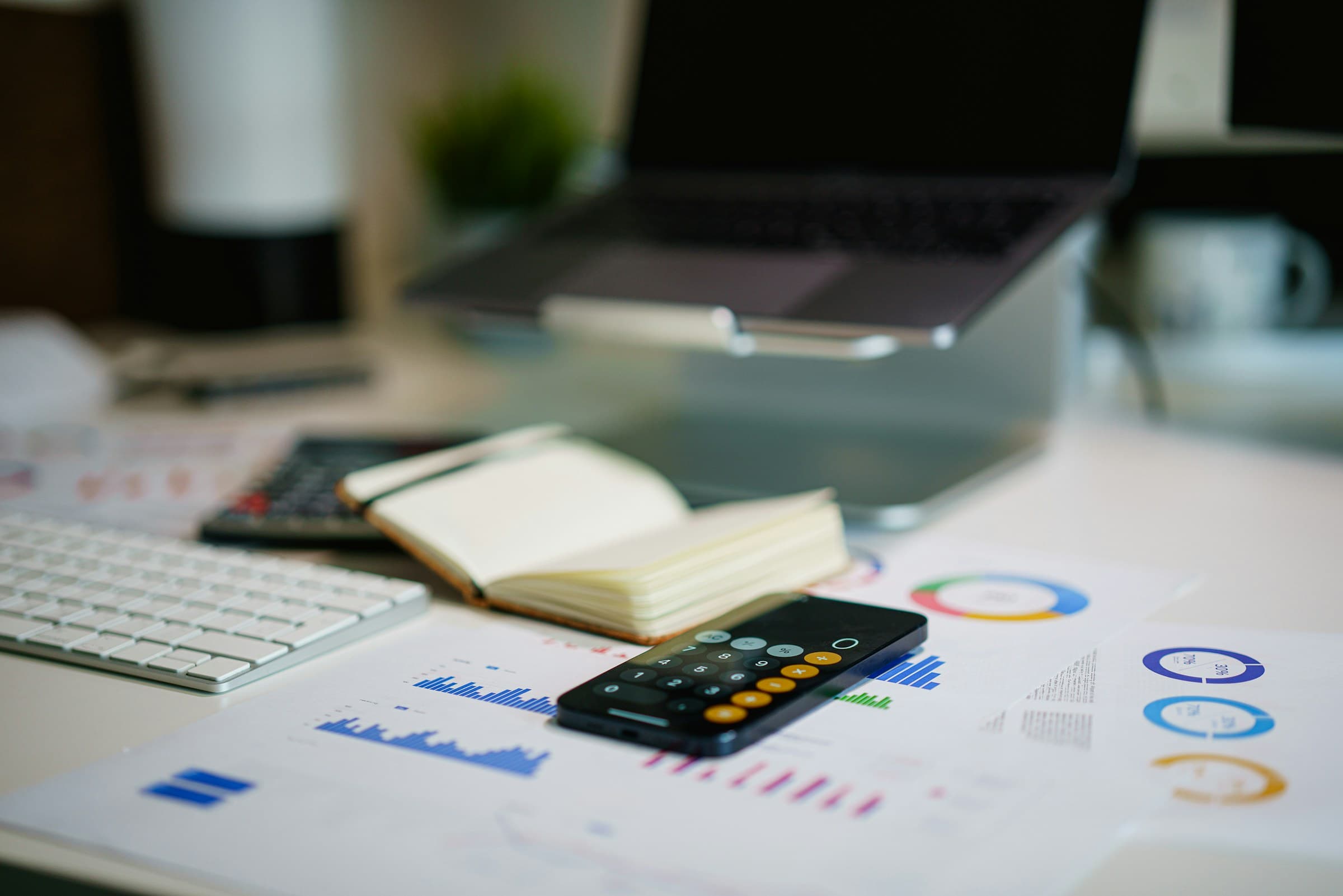 Escritorio de trabajo con un portátil, una calculadora y gráficos financieros en color